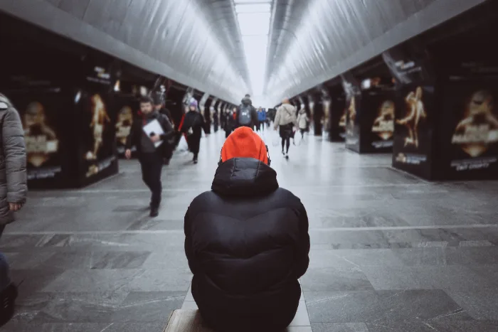 A person sitting alone in a busy station, seen from behind